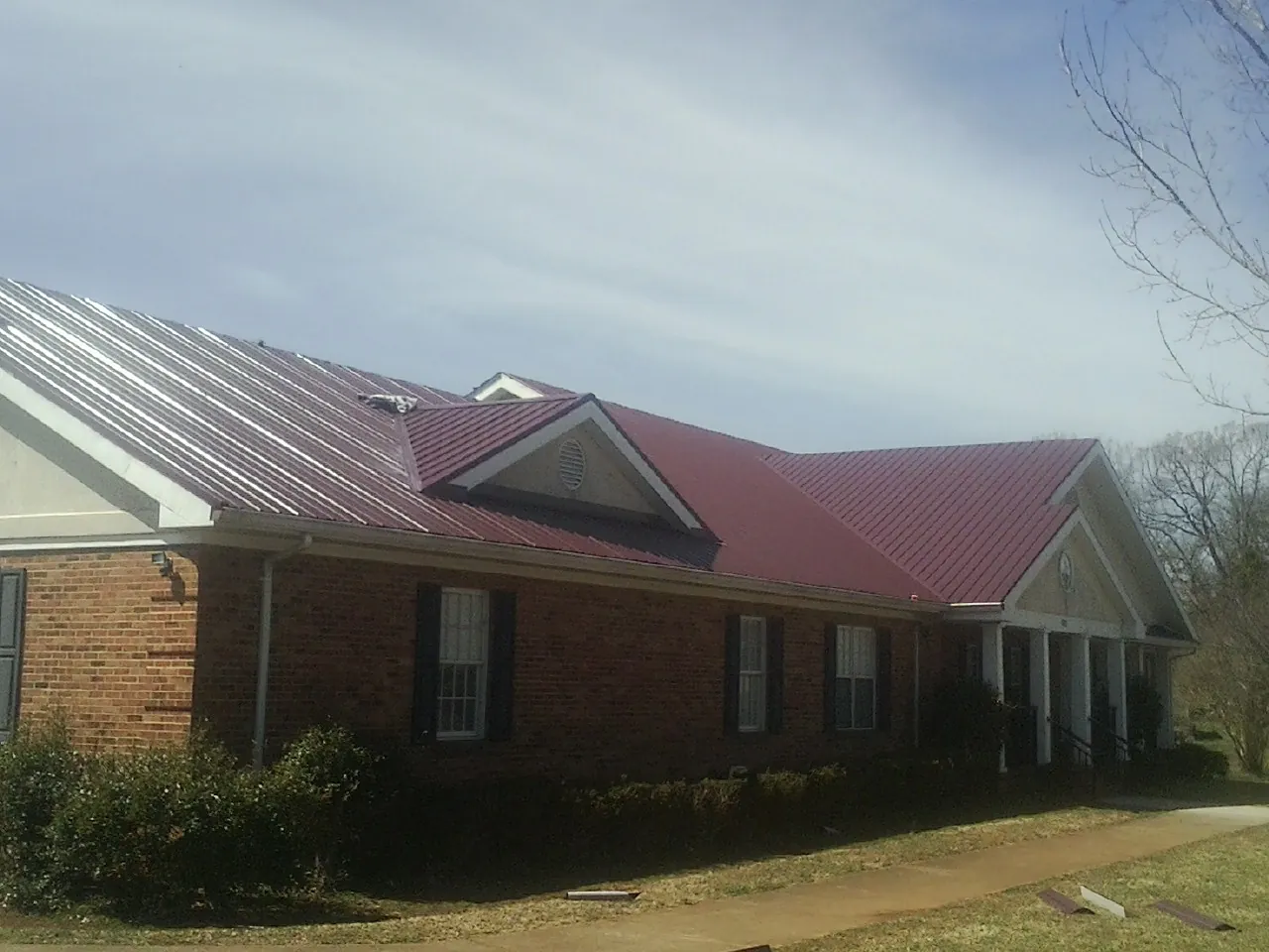 Red metal roof with gabled entries on a long brick building, from a Hail Damage Roof Repair job in Bear River City