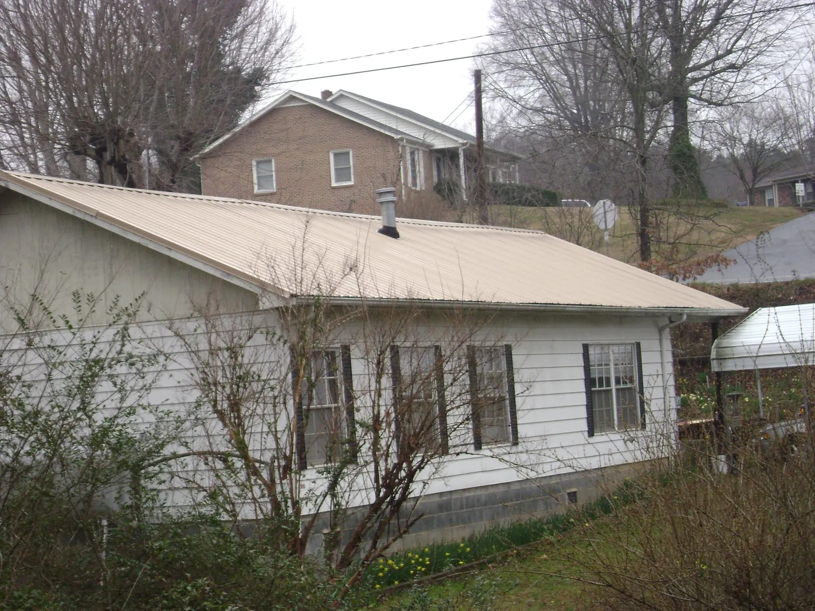 Tan metal roof on a white sided house set into a hillside — Commercial Roofing by Roofing Brothers in Bear River City